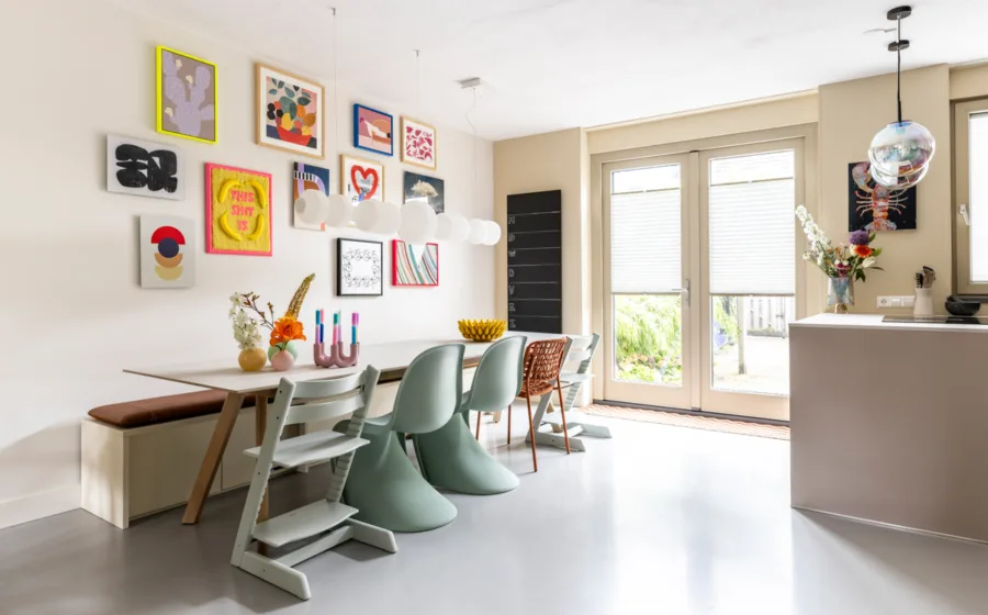 Collage van kleurrijke schilderijen op de muur zorgen voor een knusse eetkamer met bijpassende vazen op tafel.
