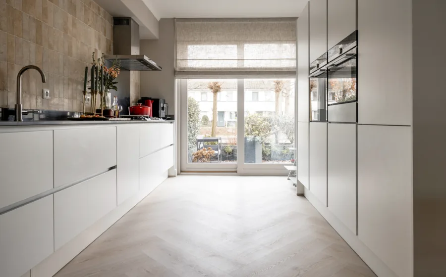 Witte keuken met beukenhouten visgraat pvc-vloer en gezellige vouwgordijnen voor een knusse sfeer.