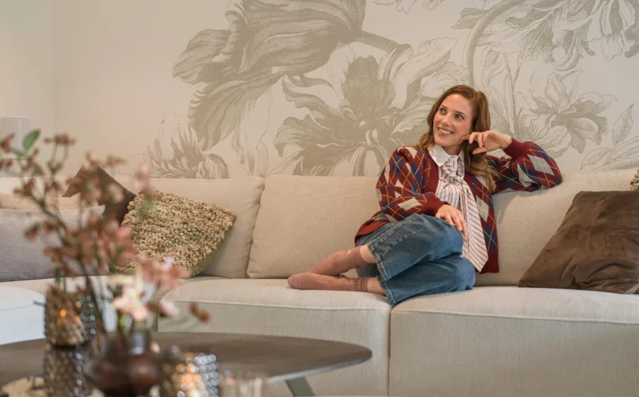 Vrouw op lichte bank met licht bloemen behang op de muur