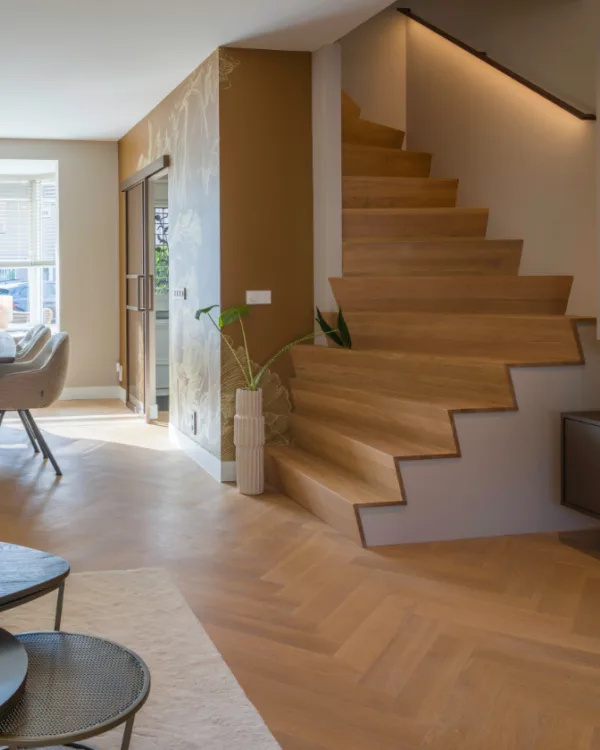 Woonkamer met visgraat vloer, haard, zithoek en Z-trap design trap met LED trapverlichting.