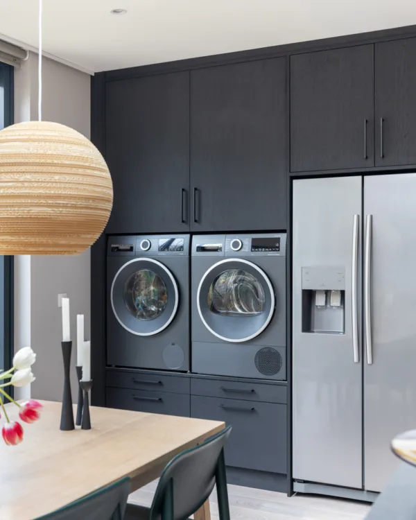 Een woonkeuken met mat zwarte wandkast op maat, met wasmachine en koelkast als onderdeel van de kast. Uit vtwonen in Amsterdam, samenwerking met Aanhuis.nl