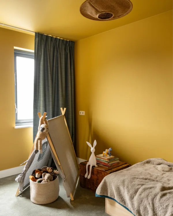 Gele muren en plafond in kinderkamer met lichtgroen tapijt en blauwe overgordijnen