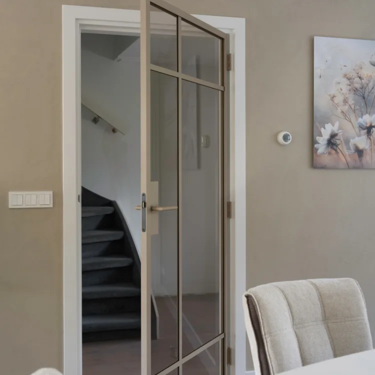 Eetkamer met witte tafel en stoelen en stalen deur naar de hal voor meer daglicht en een ruimtelijk gevoel.