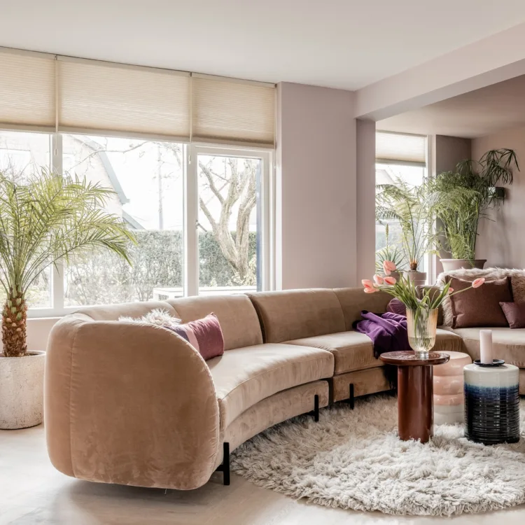 Woonkamer met lichte plisségordijnen met degradee effect; een kleurverloop van licht naar donker. Past perfect bij de fluwelen bank en lichte vloer.